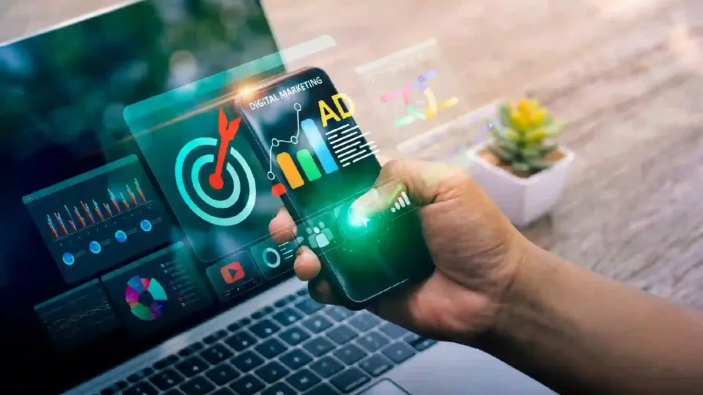 Hand holding a smartphone displaying holographic marketing analytics and colorful charts over a laptop keyboard.