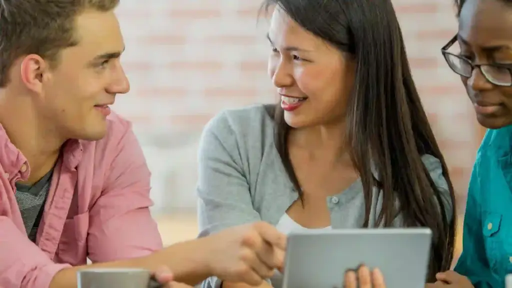 Three coworkers smiling at a tablet during a casual team discussion for a project.
