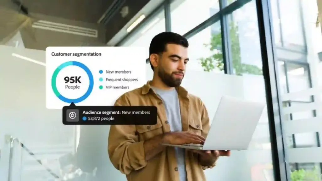 Man standing with a laptop in a glass-walled office; a floating infographic reads 'Customer segmentation' and shows 95K people with segments: New members, Frequent shoppers, VIP members.