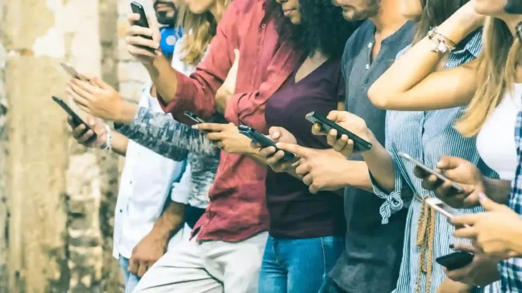 Group of friends standing side by side, each looking at and using smartphones outdoors near a stone wall.