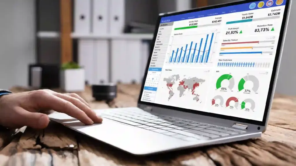 Person typing on a laptop displaying a colorful analytics dashboard with charts and a world map on screen.