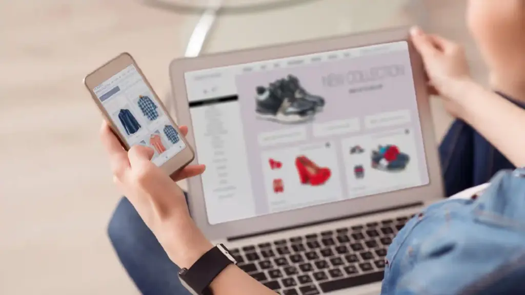 Person browsing an online fashion store on a tablet while holding a smartphone showing clothing items.