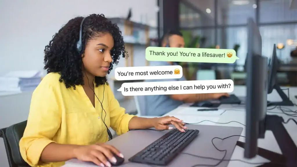 Woman wearing a yellow blouse with a headset at a computer, chat bubbles visible on the screen.