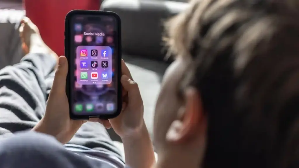 Person lying down and holding a smartphone showing a folder labeled 'Social Media' with app icons on screen.