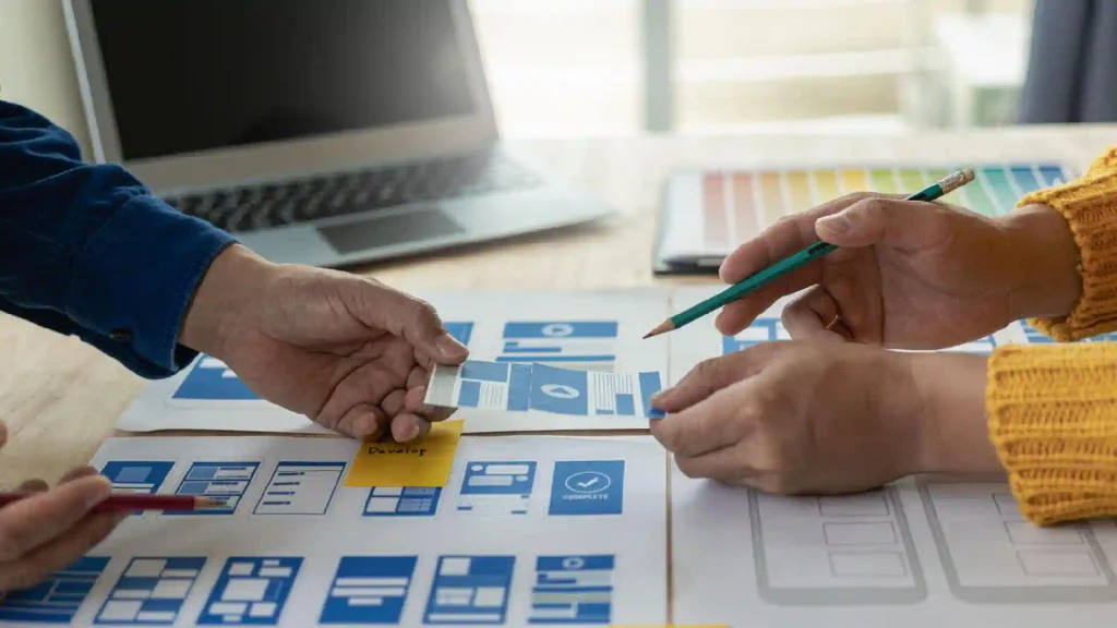 Two people collaborate on a blue UI design board with sticky notes and a pencil nearby.